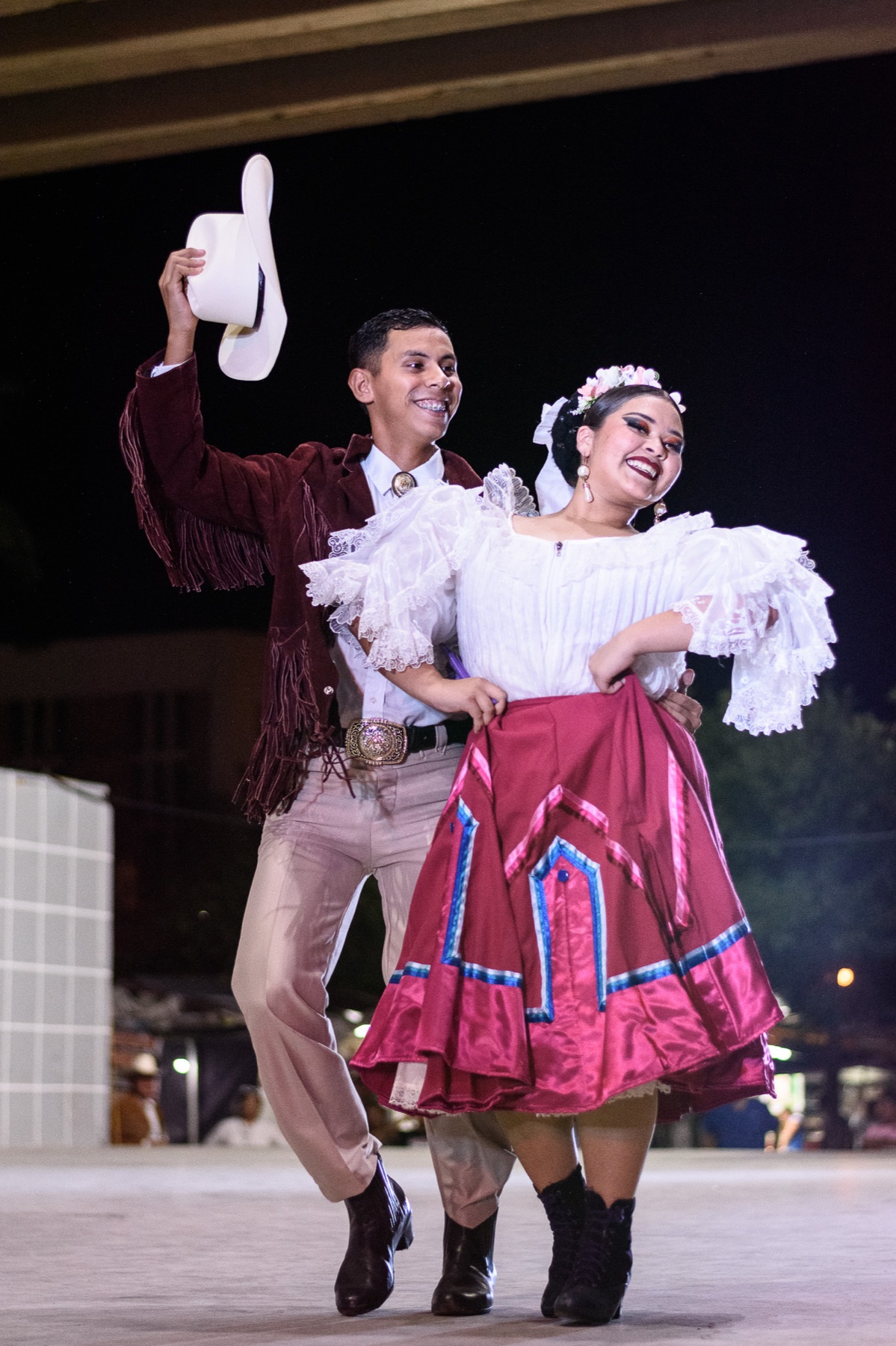 Two folk dancers from Mexico smiling during a performance, one raising a white hat