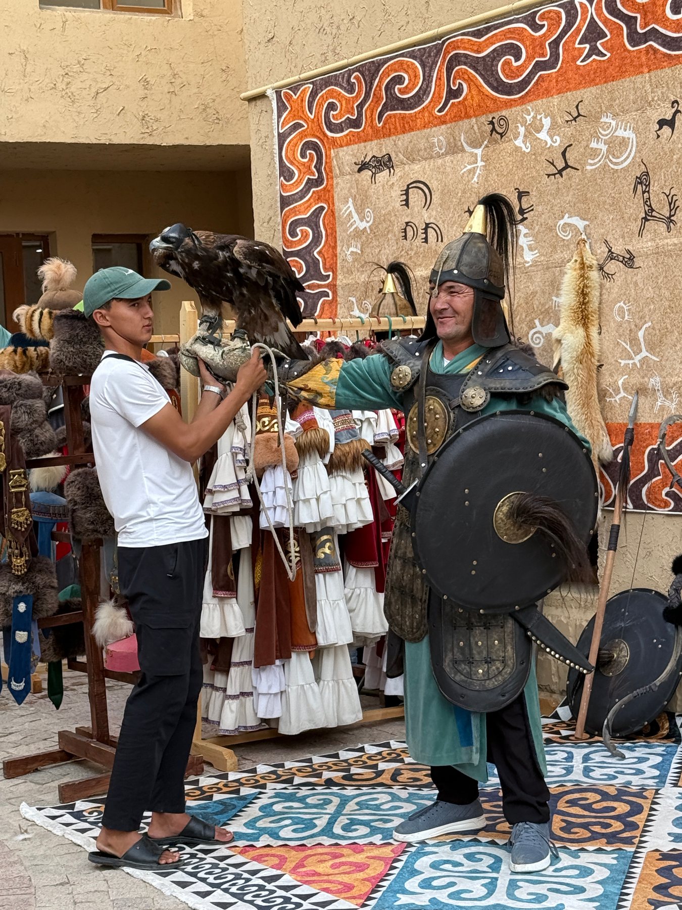 A traditionally dressed handler holding a large eagle before a display of patterned felt.