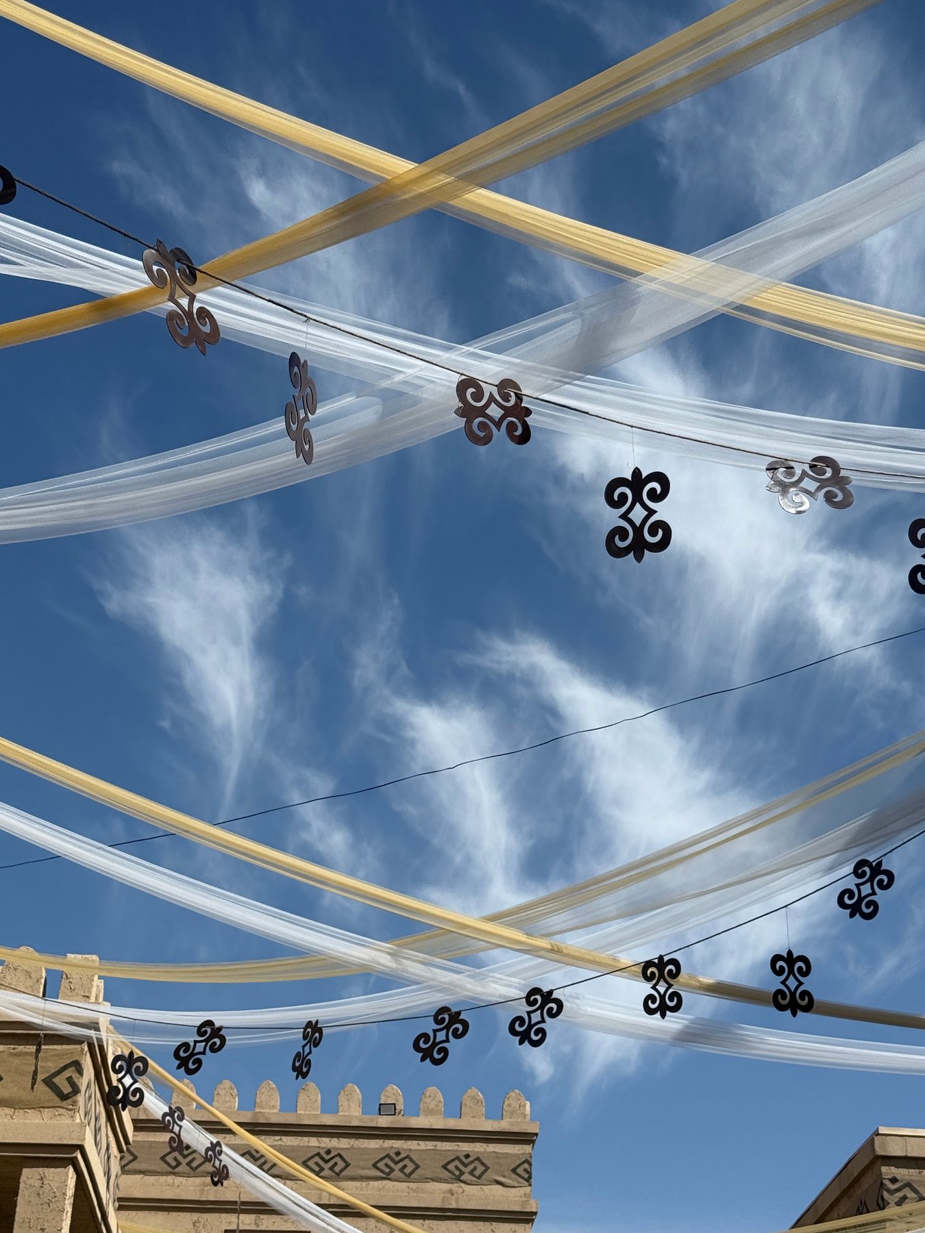 White festival streamers and dark ornamental motifs suspended against a vivid blue sky.