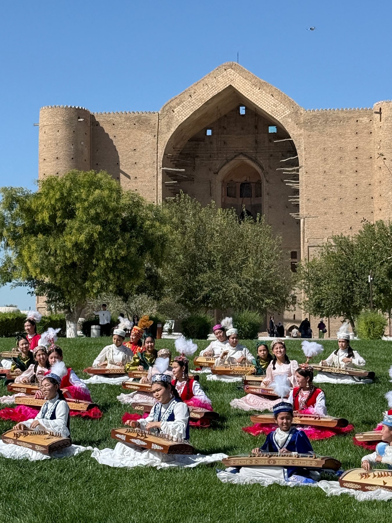 Traditional instrumentalists performing on a lawn before a monumental brick façade.