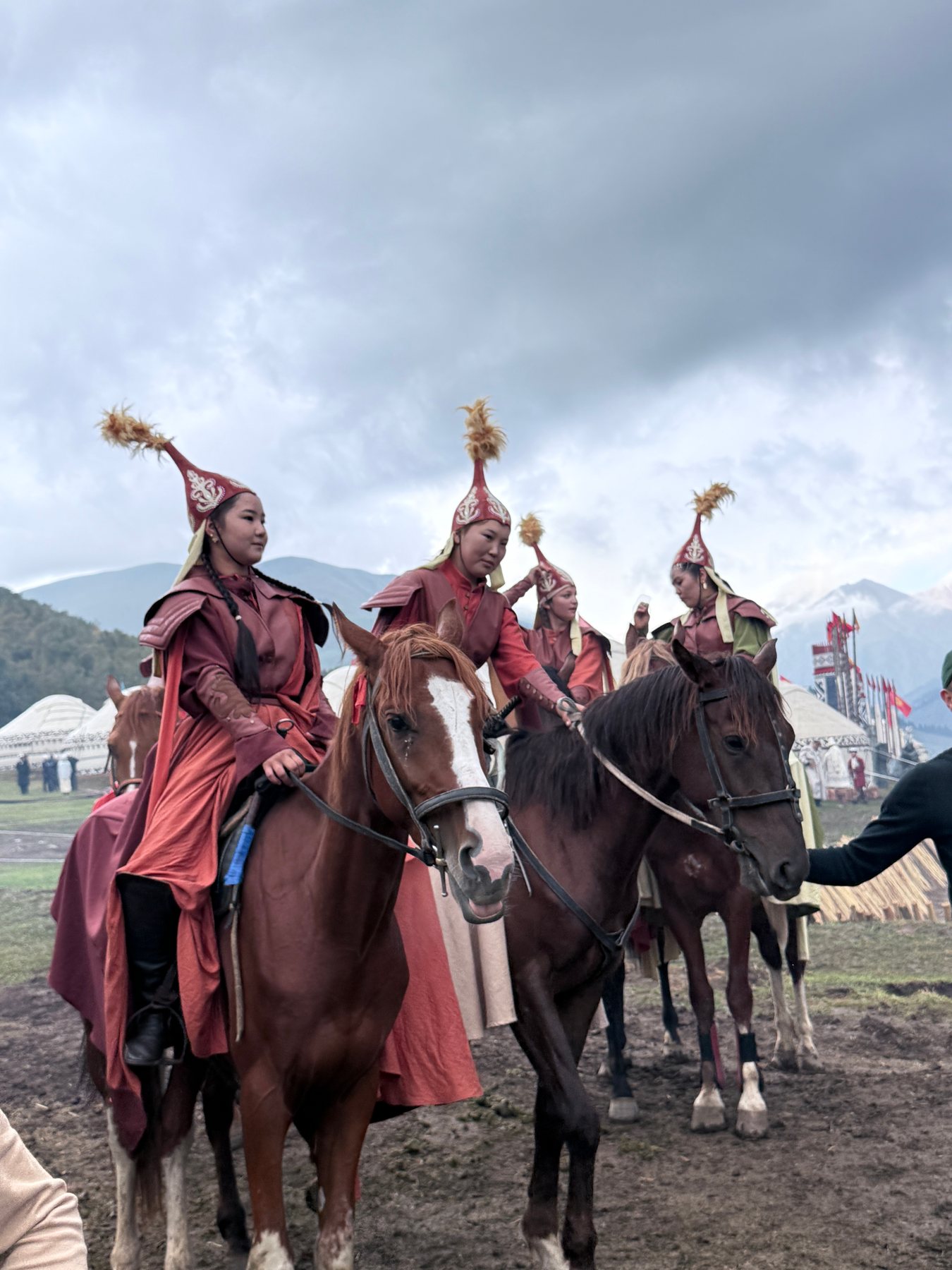 Four mounted participants in red dress with yurts and mountains behind them in Kyrgyzstan.