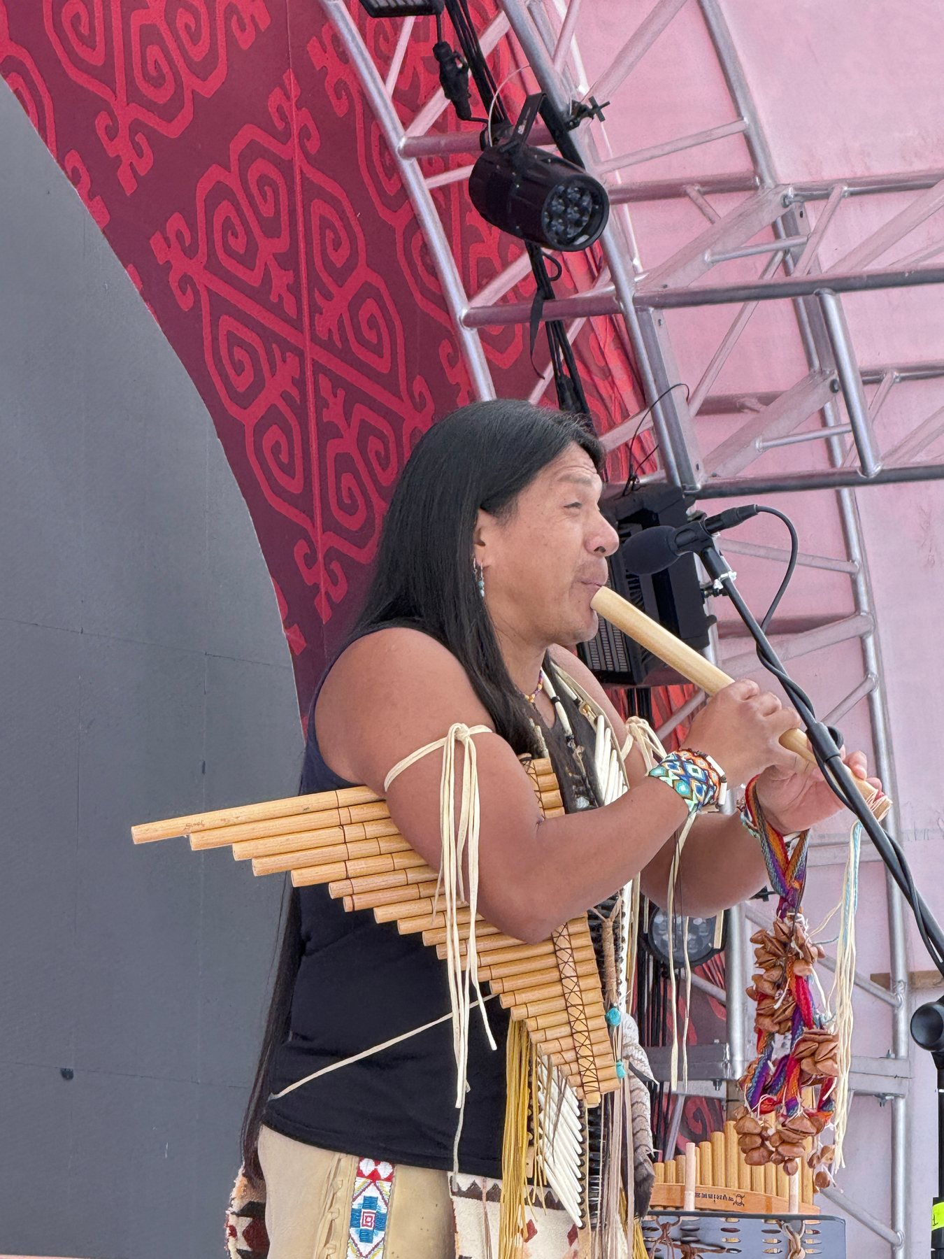 A visiting musician performing on a pan flute before a red stage wall.