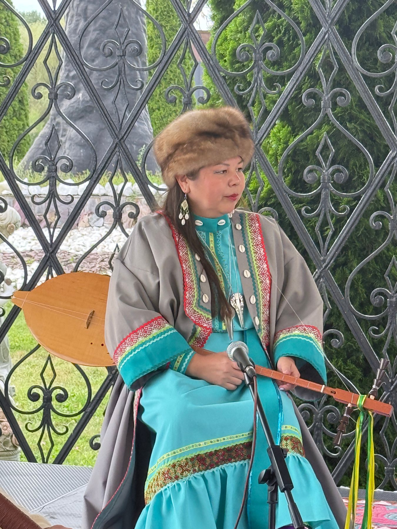 A musician in turquoise dress performing with a string instrument beside a microphone.