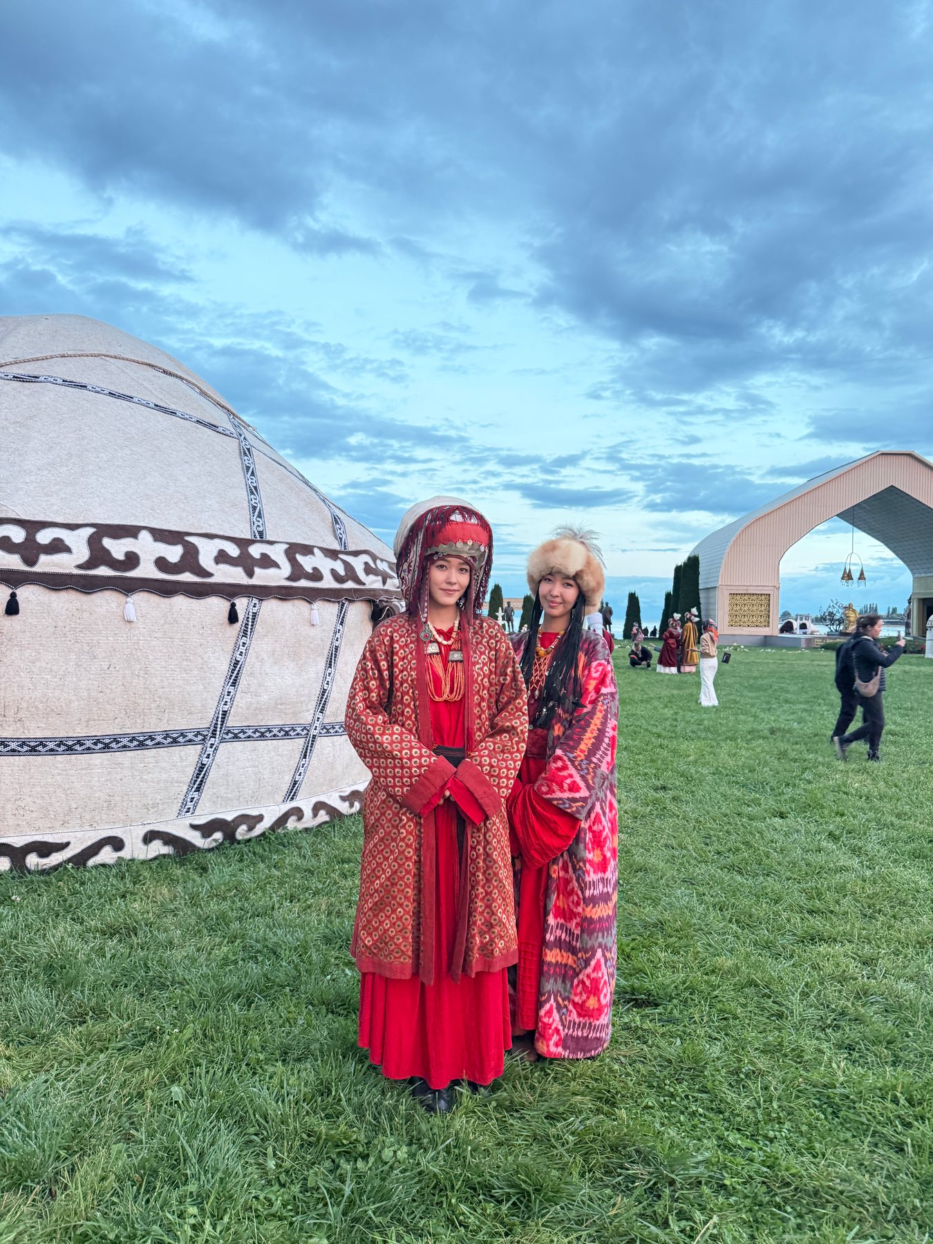 Two young women in red dress standing beside a white yurt at twilight.