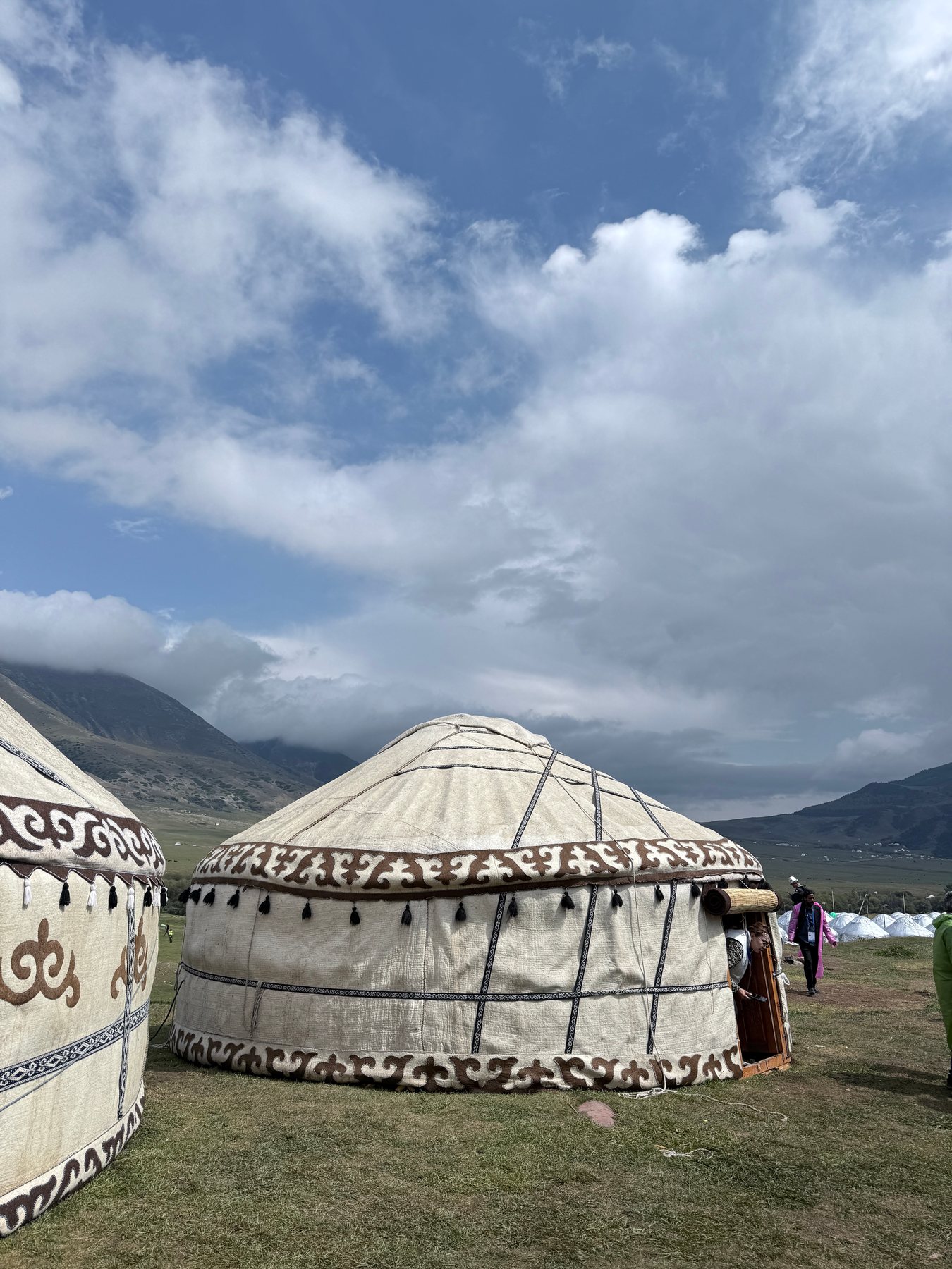 Decorated white yurts beneath a cloud-filled mountain sky.