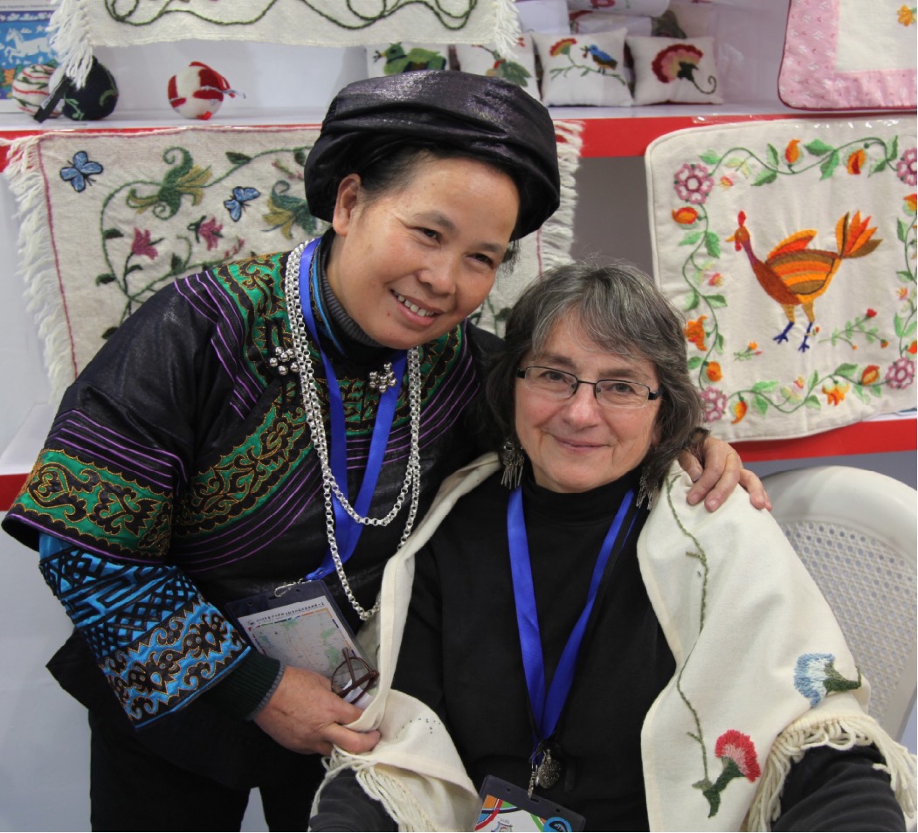 Two cultural delegates together in front of embroidered textiles.