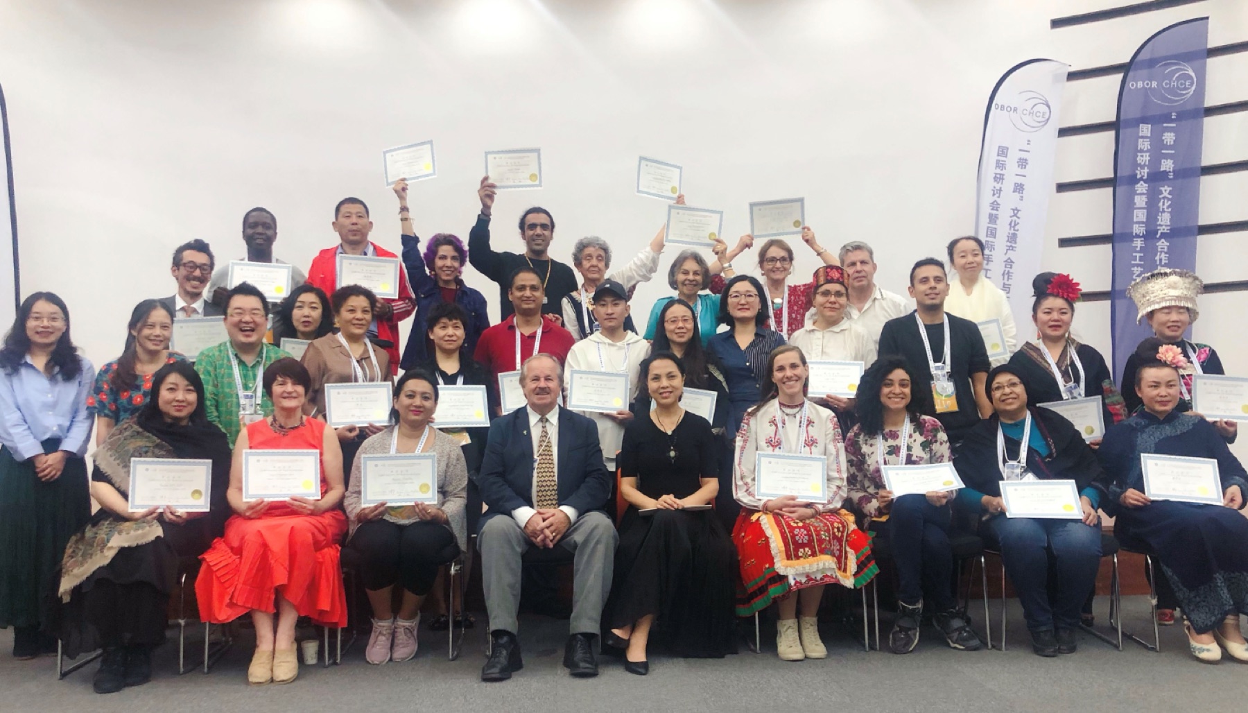 A large international group poses together while many participants hold up certificates.