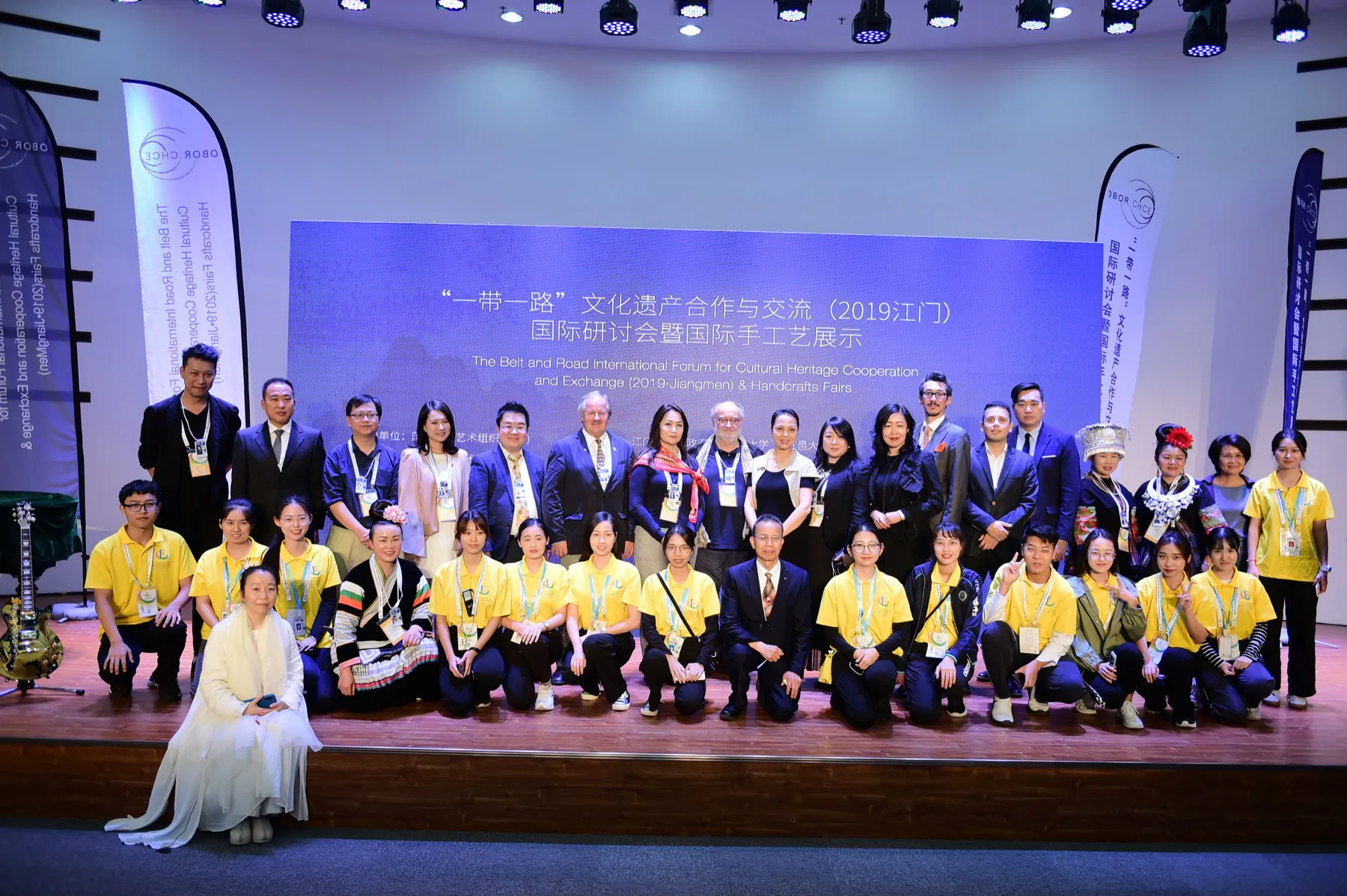 Forum participants and volunteers pose together onstage beneath the 2019 Jiangmen cultural heritage forum title.