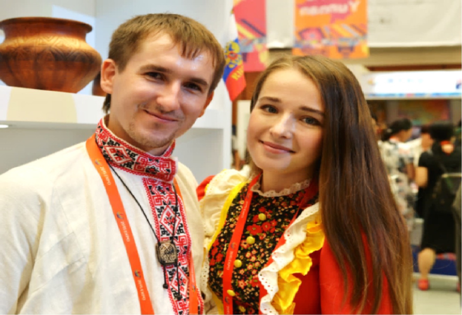 A young man and woman in embroidered clothing wear event badges at a cultural gathering.