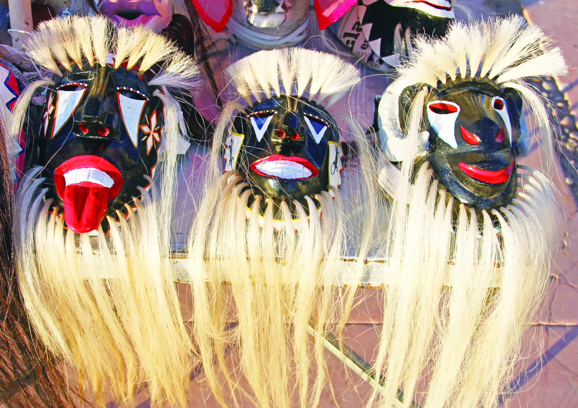 Three dark painted masks with white horsehair elements displayed together